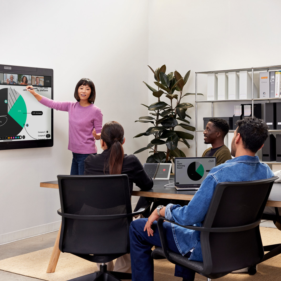 4 colleagues in a conference room video conference with one presenting at a large digital whiteboard