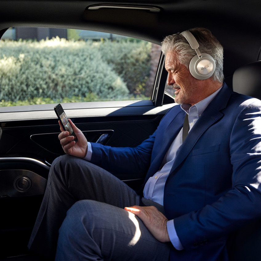 Person in a headset and suit sits in a car, chatting with colleagues on his mobile phone.