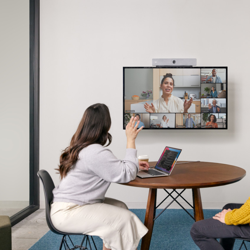 Two colleagues in a small meeting room video conference with several colleagues.